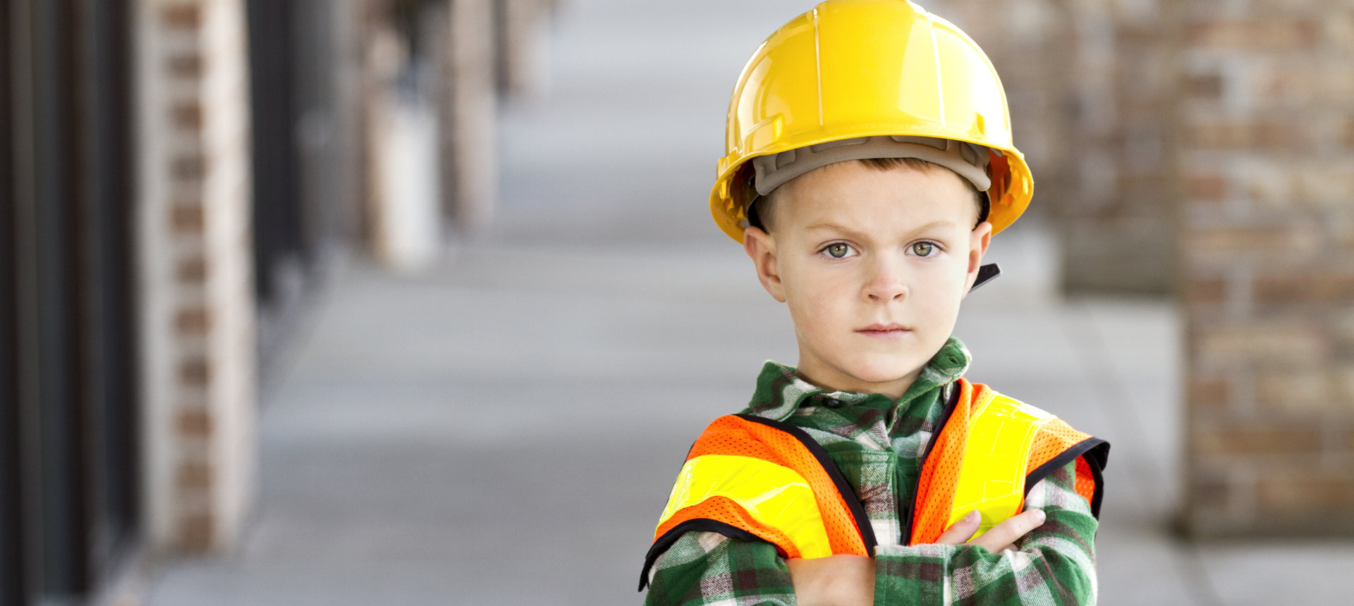 Bild von einem kleinen Jungen mit verschränkten Armen. Der junge trägt ein Holzfällerhelm mit Warnweste und einem Bauhelm. Er ist das Symbolbild für unseren Managed IT Security Service.