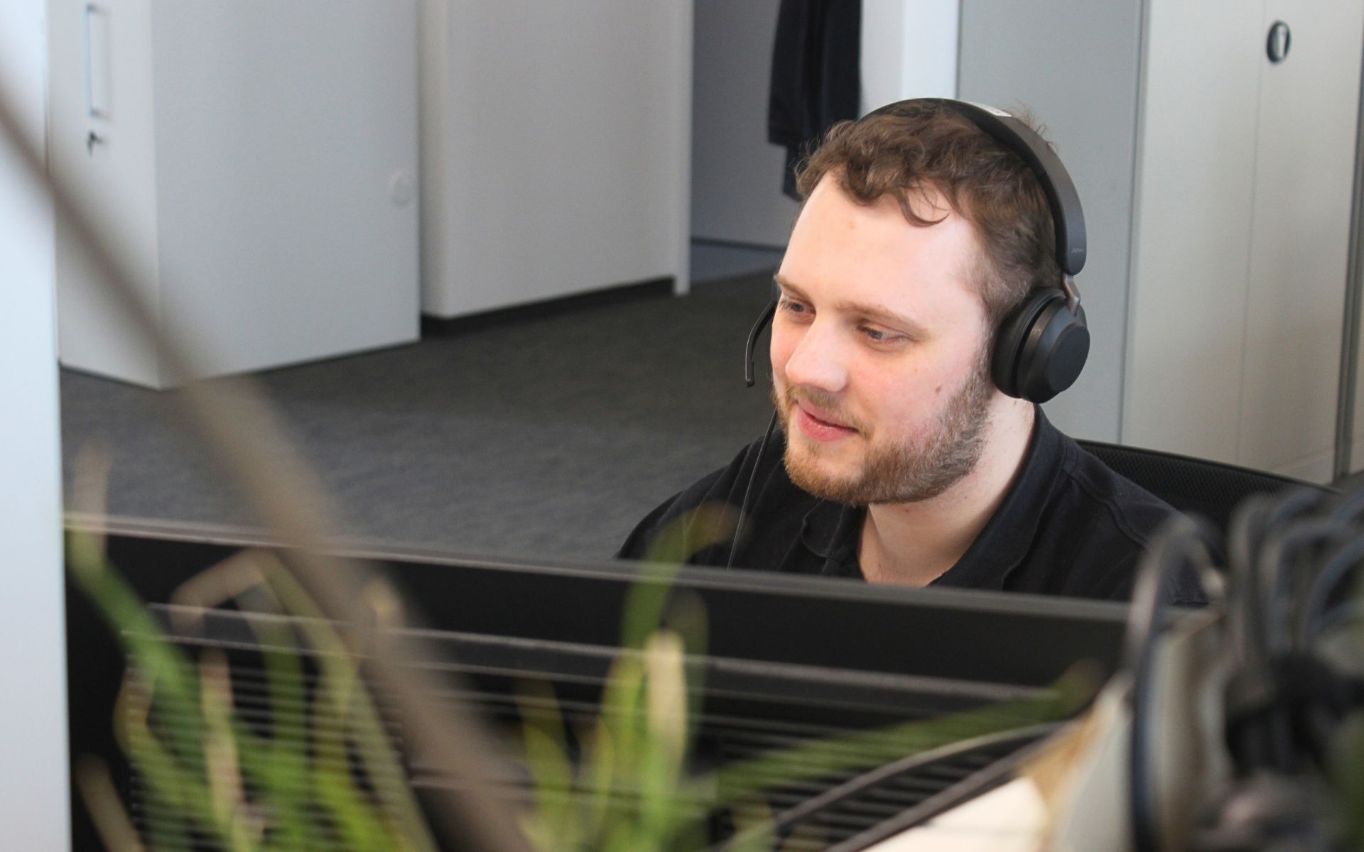 Ein Foto von einem IT-Mitarbeiter. Er arbeitet im IT User Support. Er hilft gerade einem Kunden über remote Support beim lösen eines technischen Problems.
